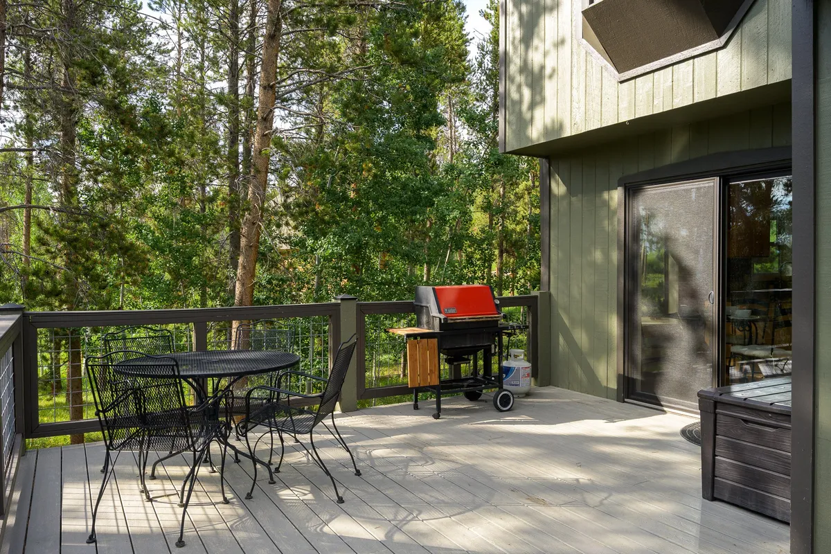 A cozy, fully fenced patio with a black wrought iron dining set and a red grill, enveloped by trees and privacy fencing. The area feels secure, perfect for children or pets to play, and invites outdoor dining in a tranquil setting.