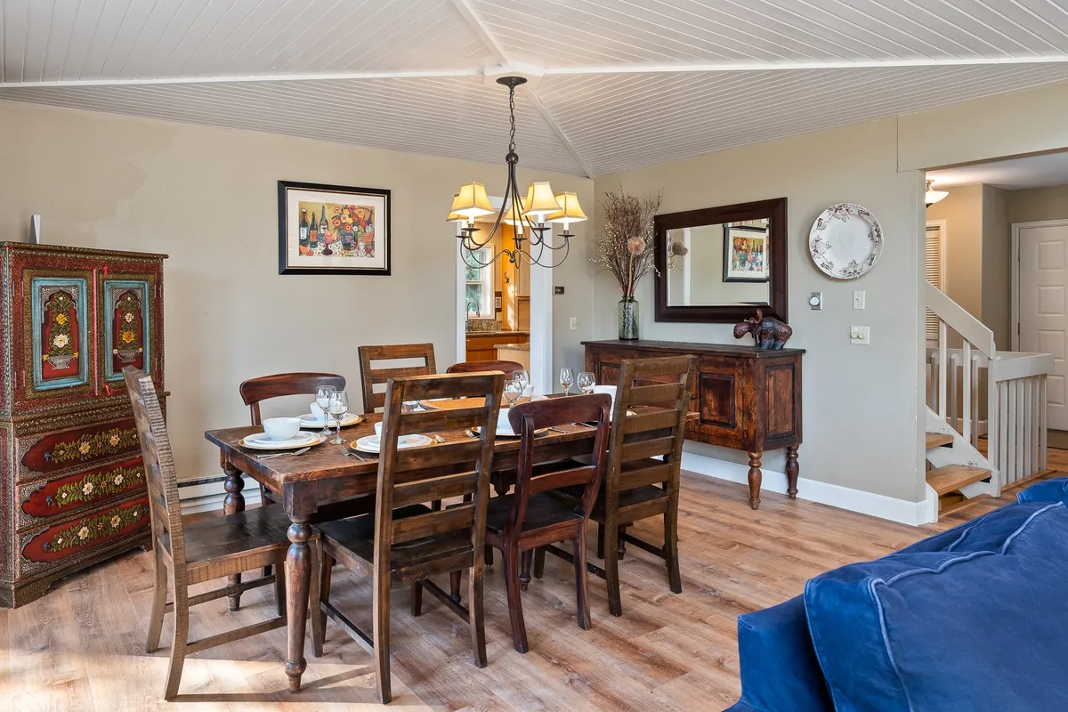 A warm and inviting dining area with a central table, colorful cabinet, chandelier, and decorative mirror. The space is set up for family dinners, entertaining guests, and holiday celebrations, creating a welcoming atmosphere for communal meals.