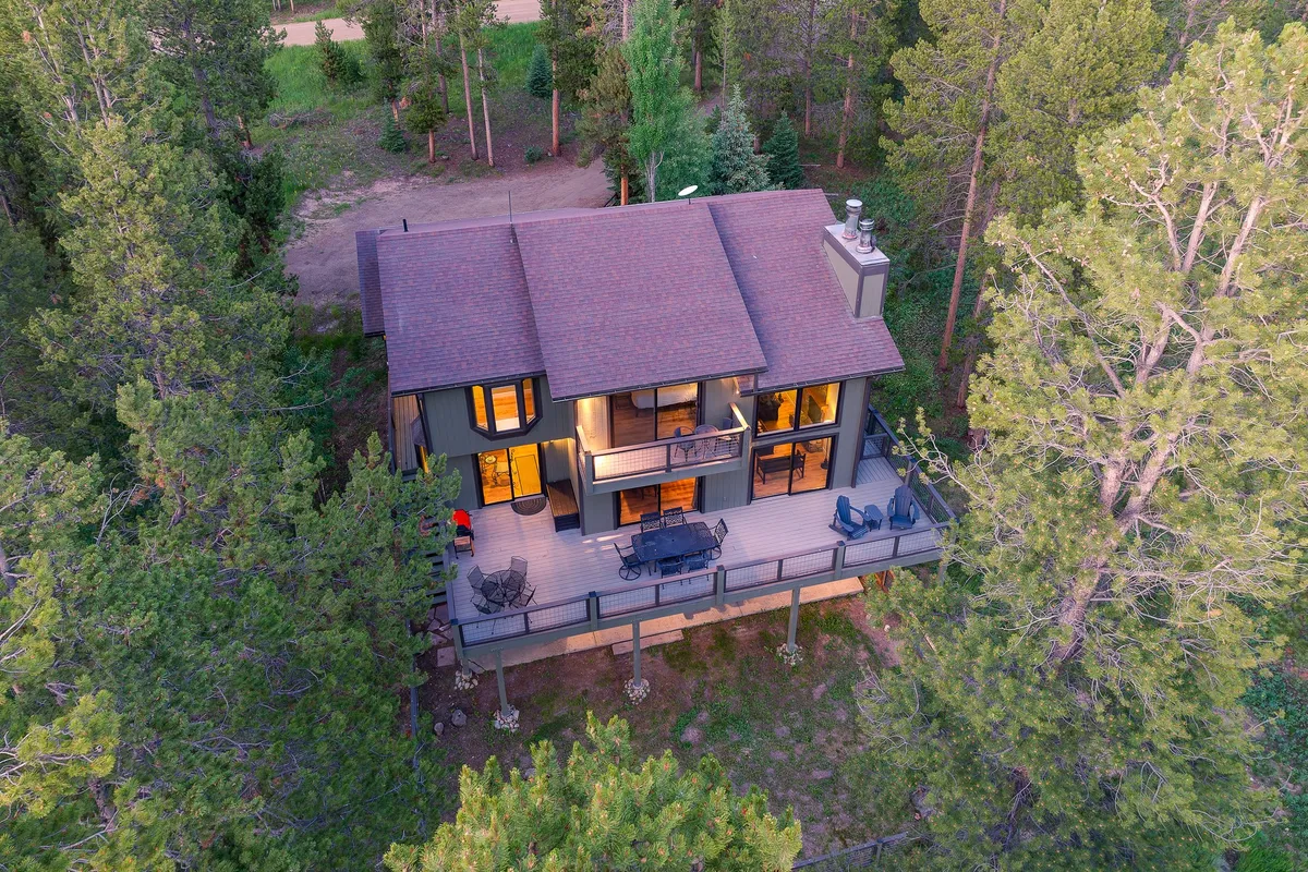 A spacious deck with comfortable seating nestled among mature trees, large windows connecting the exterior and interior, and a peaceful, natural ambiance. The deck’s vantage point offers sweeping views of the surrounding forest and hills, perfect for wildlife watching or enjoying a sunset.