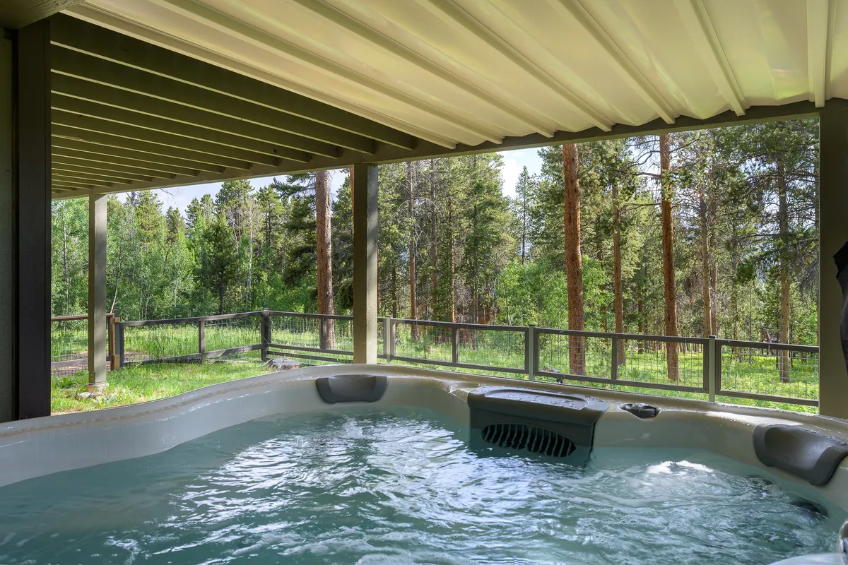 A tranquil outdoor deck featuring a modern hot tub surrounded by lush trees, with warm sunlight filtering through the leaves. The setting is private and inviting, ideal for relaxing while enjoying scenic nature views. The hot tub is the centerpiece, promising spa-style relaxation in the open air.