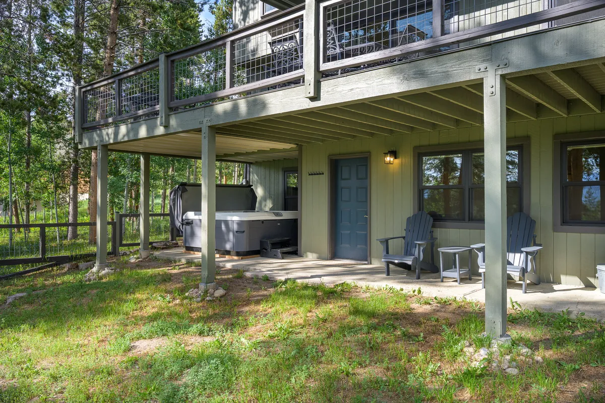 A welcoming outdoor area features a hot tub, seating area, and a wooden deck set amid lush trees. The tranquil scene is perfect for relaxing after outdoor activities, socializing with friends, or enjoying the mountain air.