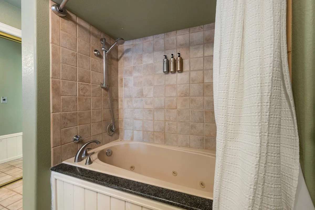A tranquil bathroom featuring a deep soaking bathtub, tiled walls, and soap dispensers. The lighting and design evoke a relaxing, high-end spa experience.
