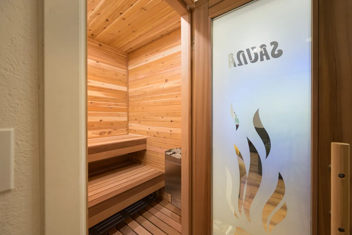 This image showcases a modern, wooden sauna with inviting benches and a clear 'Sauna' sign on frosted glass. The atmosphere is warm, calm, and perfect for unwinding after a day of adventure.