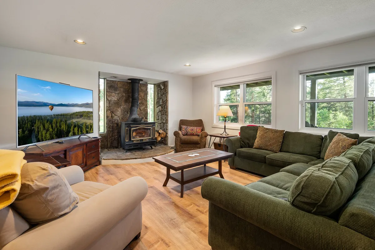 A cozy family room with a large television, a wood-burning stove, and a spacious green sectional sofa positioned to take in views from the windows. The space is designed for movie nights, game sessions, and relaxed evenings by the fire, perfectly supporting social gatherings and entertainment.