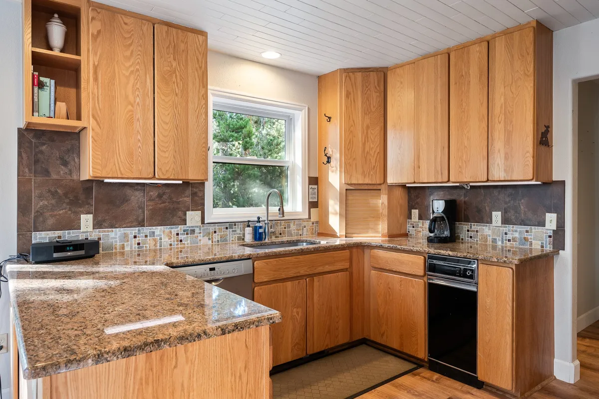 A chef-inspired kitchen with granite countertops, rich wood cabinetry, a colorful backsplash, and a window for natural light. The kitchen is designed for cooking, entertaining, and gathering, featuring modern amenities and an open layout ideal for group meal preparation.